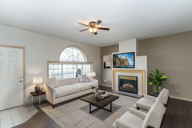 living room with a tiled fireplace, ceiling fan, light wood-type flooring, and a textured ceiling