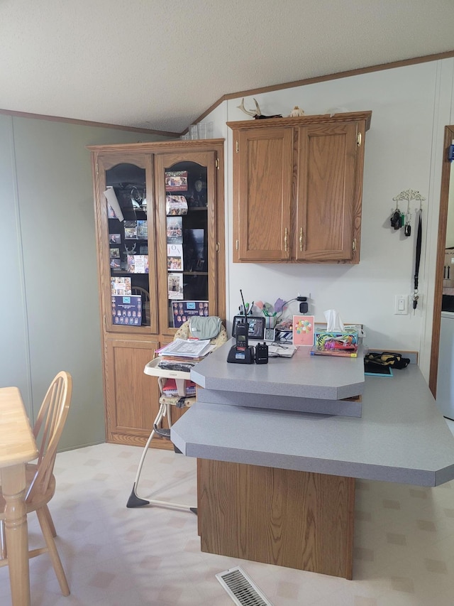 kitchen featuring visible vents, brown cabinets, a peninsula, crown molding, and a textured ceiling