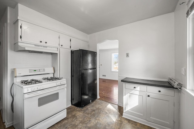 kitchen featuring freestanding refrigerator, white gas range oven, under cabinet range hood, white cabinetry, and dark countertops