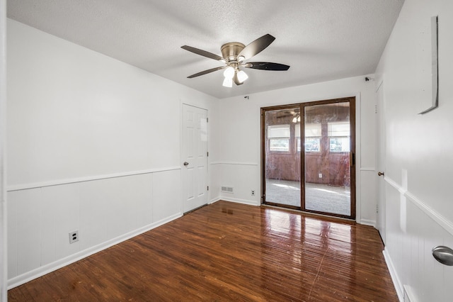 empty room with hardwood / wood-style floors, visible vents, a wainscoted wall, ceiling fan, and a textured ceiling