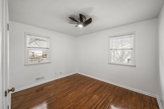 spare room featuring a wealth of natural light, visible vents, baseboards, and dark wood-style flooring