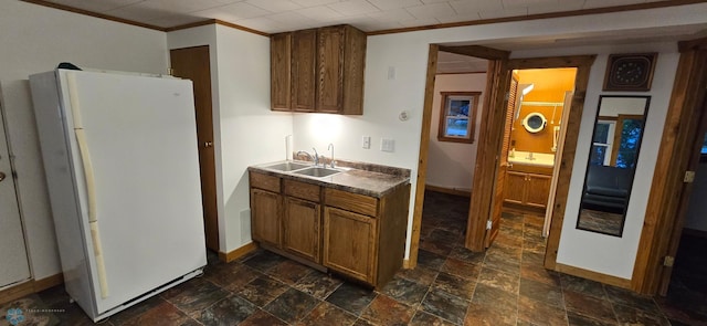 kitchen with dark countertops, brown cabinetry, freestanding refrigerator, stone finish floor, and a sink