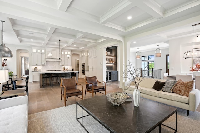 living room featuring an inviting chandelier, beam ceiling, light hardwood / wood-style flooring, and coffered ceiling