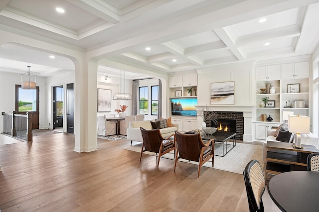 living room featuring coffered ceiling, a fireplace, beam ceiling, and light hardwood / wood-style flooring