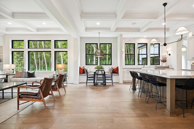 kitchen with a breakfast bar, white cabinetry, light hardwood / wood-style floors, decorative light fixtures, and beamed ceiling