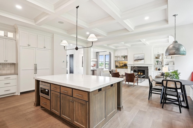 kitchen featuring white cabinetry, light hardwood / wood-style floors, a brick fireplace, decorative light fixtures, and beamed ceiling