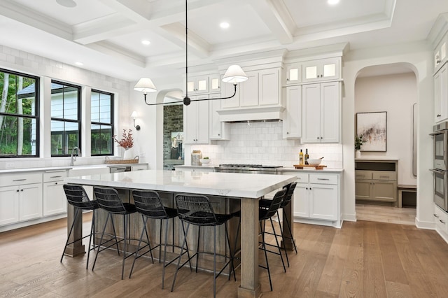 kitchen featuring white cabinetry, tasteful backsplash, light stone counters, a center island, and hanging light fixtures