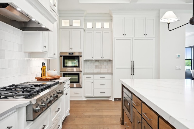 kitchen with stainless steel appliances, premium range hood, white cabinets, and light stone counters