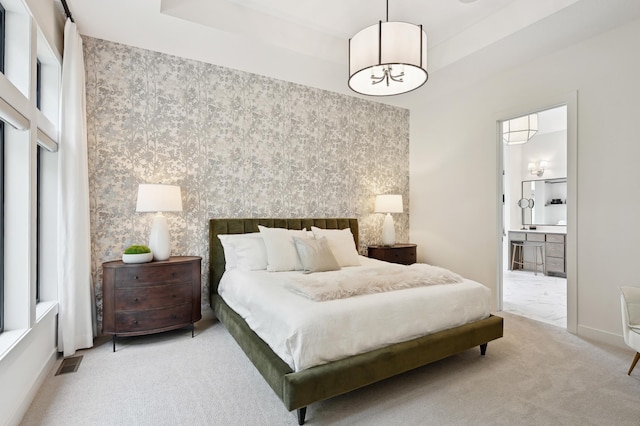 carpeted bedroom with a tray ceiling and ensuite bathroom