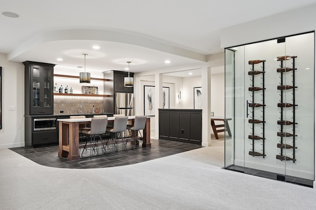 bar featuring tasteful backsplash, appliances with stainless steel finishes, hanging light fixtures, and dark colored carpet