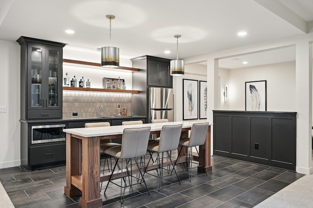 bar with tasteful backsplash, hanging light fixtures, sink, and appliances with stainless steel finishes