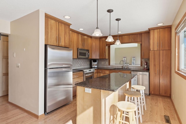 kitchen with hanging light fixtures, a center island, sink, backsplash, and appliances with stainless steel finishes