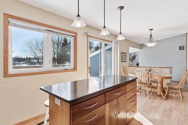 kitchen with light wood-type flooring, a textured ceiling, hanging light fixtures, and a center island