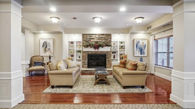 living area with a stone fireplace, wood finished floors, visible vents, and ornate columns