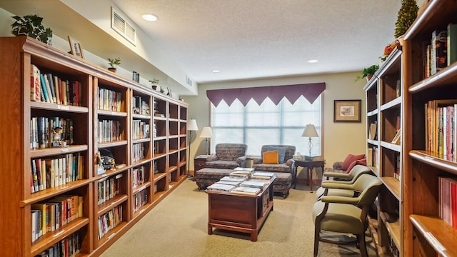 living area featuring a textured ceiling, recessed lighting, carpet floors, visible vents, and wall of books