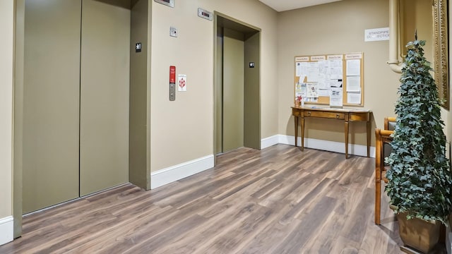 hall with baseboards, wood finished floors, and elevator