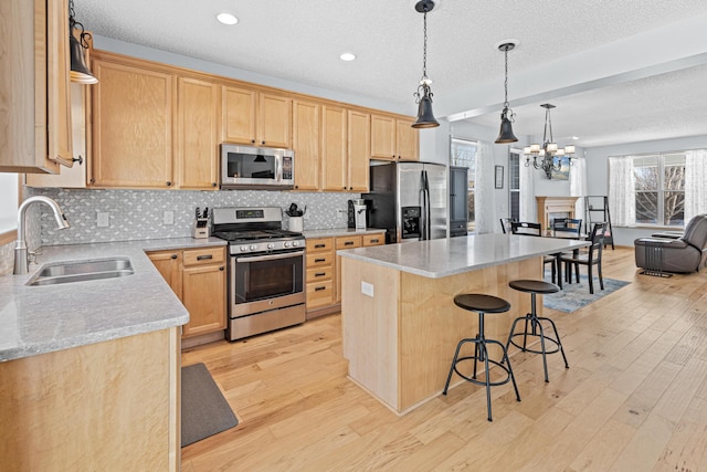 kitchen with sink, light wood-type flooring, a kitchen island, stainless steel appliances, and light stone countertops