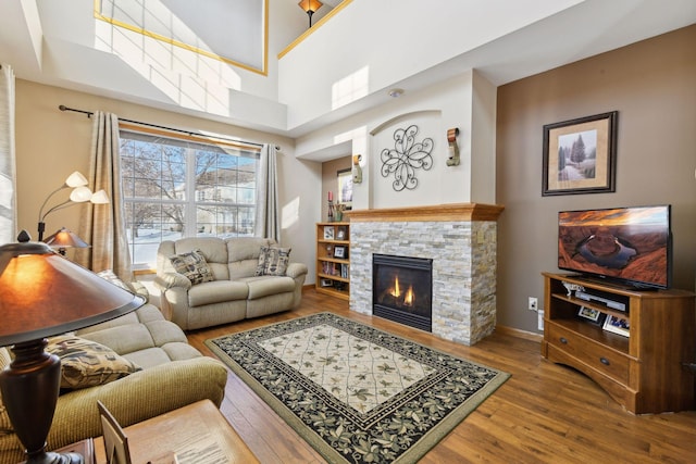 living room with a towering ceiling, wood-type flooring, and a stone fireplace