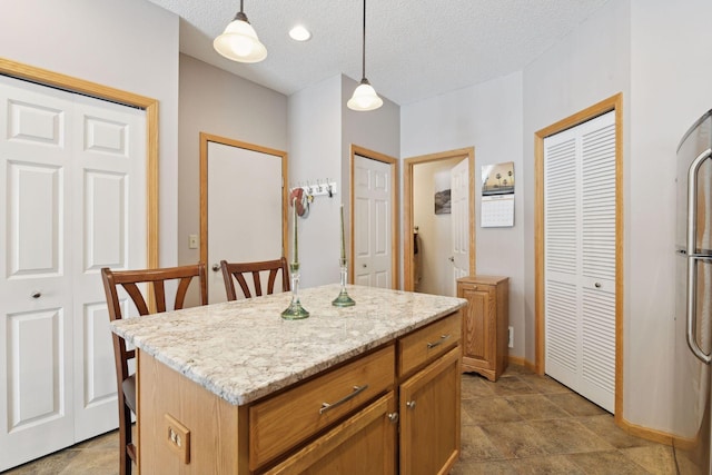 kitchen with a center island, hanging light fixtures, a textured ceiling, stainless steel refrigerator, and light stone countertops