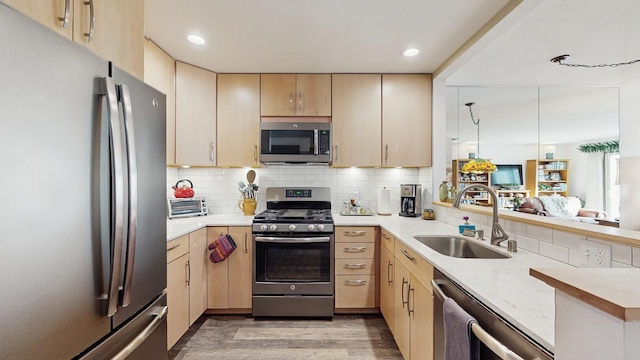 kitchen with a peninsula, appliances with stainless steel finishes, a sink, and light brown cabinetry