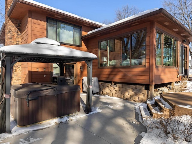 snow covered rear of property with a hot tub