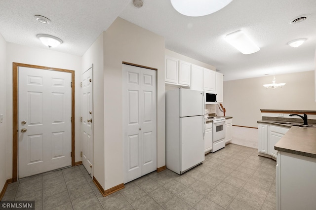 kitchen with sink, white appliances, white cabinetry, hanging light fixtures, and a textured ceiling