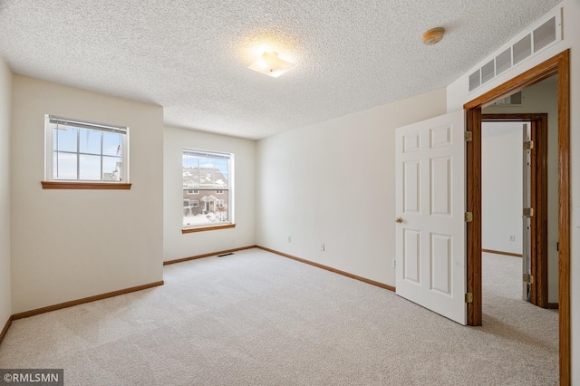 spare room featuring light colored carpet and a textured ceiling