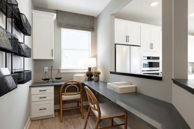 office featuring baseboards, built in study area, and light wood finished floors