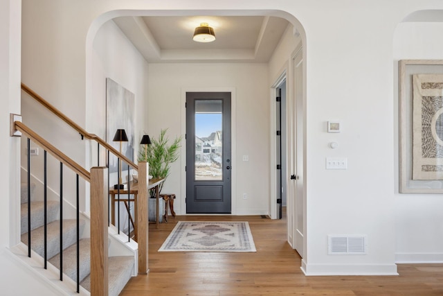 entryway featuring baseboards, visible vents, arched walkways, a raised ceiling, and light wood-type flooring