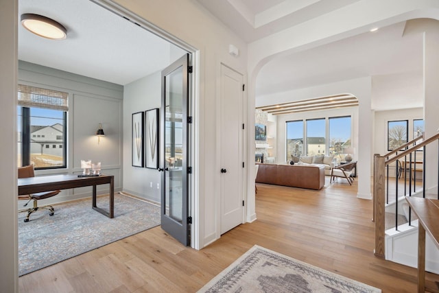 home office with baseboards, arched walkways, and light wood finished floors