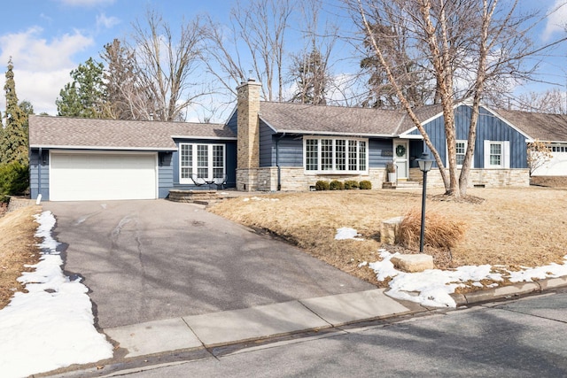 ranch-style house featuring a chimney, a shingled roof, a garage, stone siding, and aphalt driveway