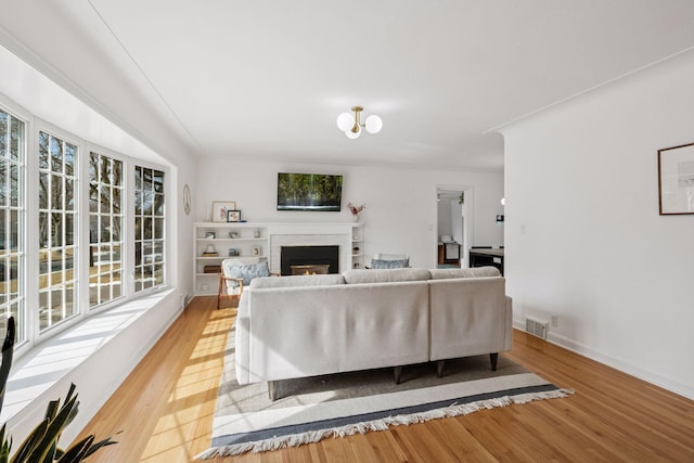 living area with visible vents, a fireplace, light wood-style floors, and baseboards