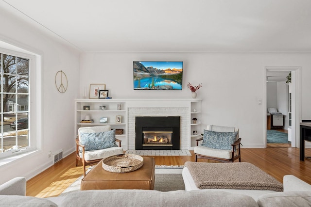 living area with a fireplace, wood finished floors, visible vents, and baseboards