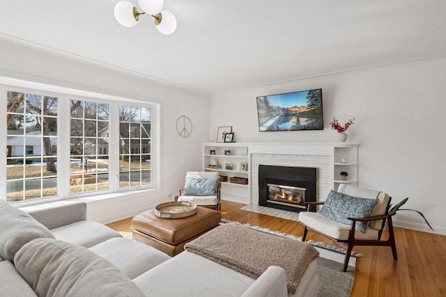 living room with a brick fireplace, light wood-style flooring, and baseboards