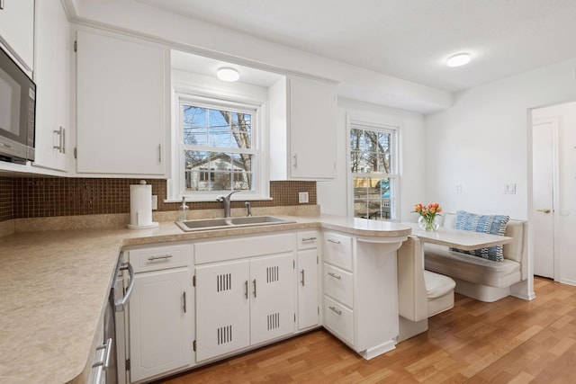 kitchen with a sink, white cabinetry, light wood-style floors, light countertops, and decorative backsplash