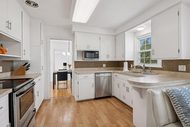 kitchen featuring visible vents, light wood-type flooring, open shelves, a sink, and appliances with stainless steel finishes