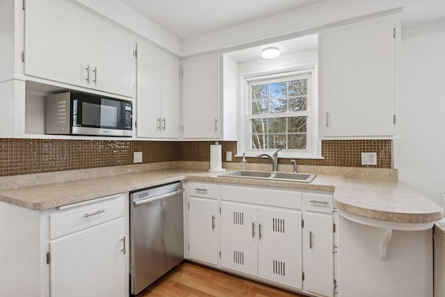 kitchen featuring light wood-type flooring, a sink, tasteful backsplash, appliances with stainless steel finishes, and light countertops