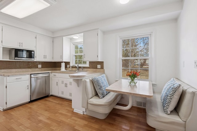 kitchen with light wood-style flooring, stainless steel appliances, decorative backsplash, light countertops, and white cabinets