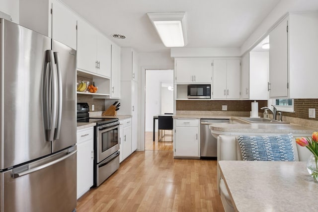 kitchen with backsplash, light wood finished floors, appliances with stainless steel finishes, and a sink