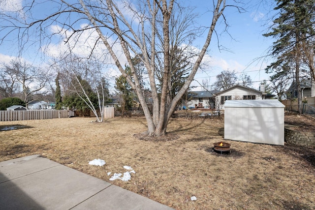 view of yard featuring a fire pit, a storage unit, an outdoor structure, and fence