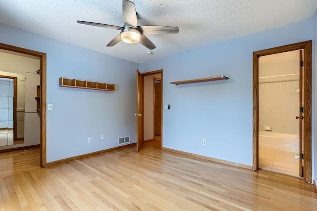 unfurnished bedroom with a walk in closet, light hardwood / wood-style flooring, a textured ceiling, and ensuite bathroom