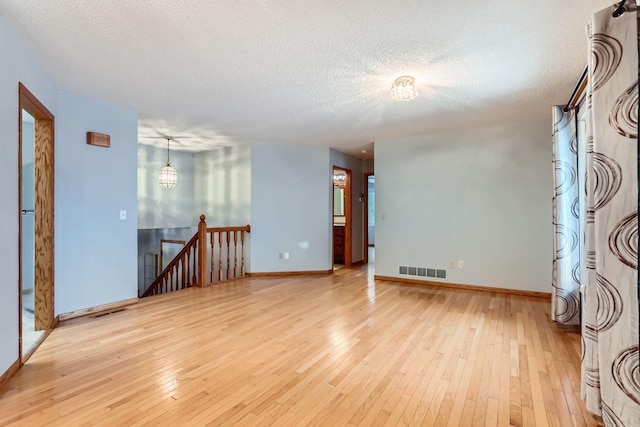 spare room featuring a textured ceiling and light hardwood / wood-style floors