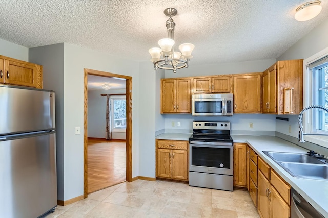 kitchen featuring pendant lighting, sink, appliances with stainless steel finishes, an inviting chandelier, and a textured ceiling