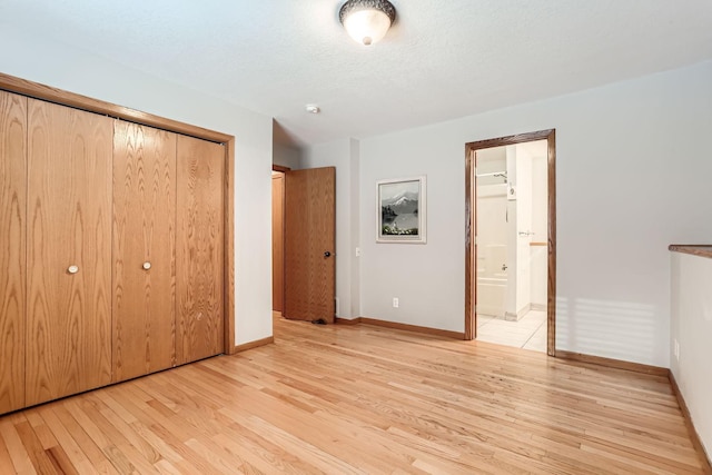 unfurnished bedroom featuring a closet, ensuite bathroom, a textured ceiling, and light hardwood / wood-style flooring