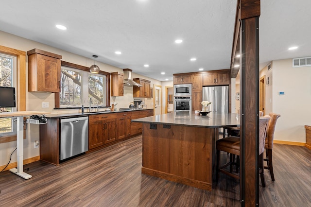 kitchen with stainless steel appliances, a sink, a kitchen island, visible vents, and wall chimney range hood