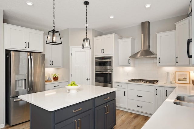 kitchen with stainless steel appliances, hanging light fixtures, wall chimney range hood, and white cabinets