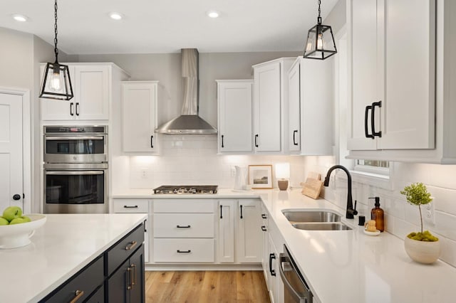 kitchen featuring sink, white cabinetry, hanging light fixtures, stainless steel appliances, and wall chimney range hood