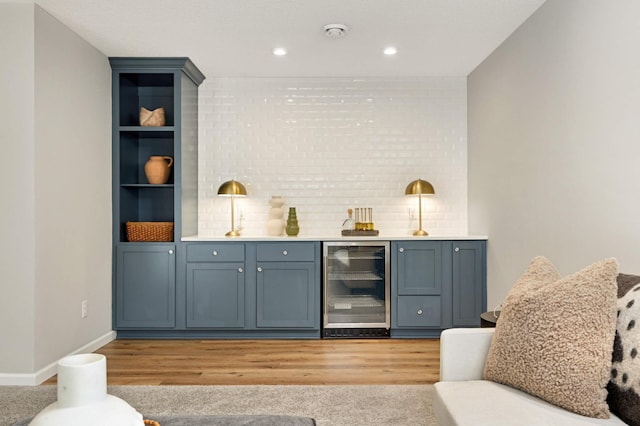 bar featuring tasteful backsplash, blue cabinets, wine cooler, and light hardwood / wood-style flooring