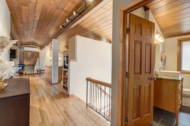 hall with a wall unit AC, lofted ceiling, a sink, wood ceiling, and light wood-type flooring