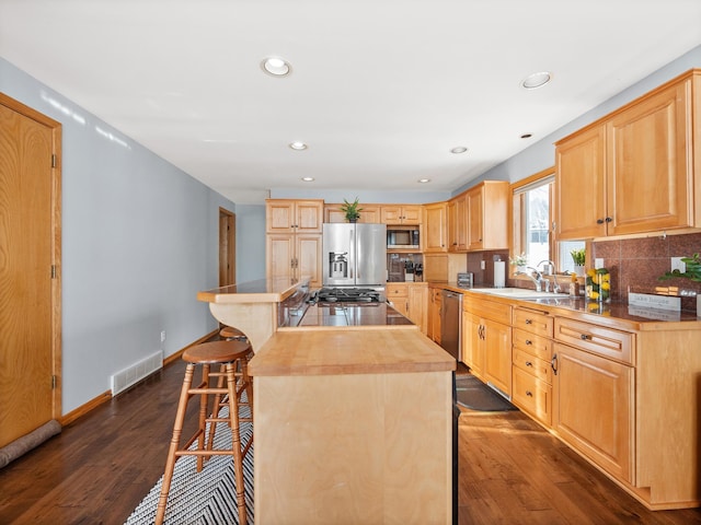 kitchen featuring a center island, a breakfast bar area, light brown cabinetry, appliances with stainless steel finishes, and a sink